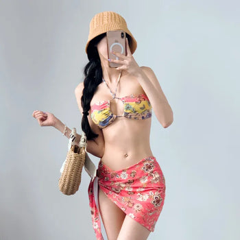 A three-piece coral orange color block floral bikini with a wrap skirt and a halter neck swimsuit that covers the body.